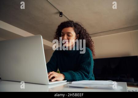 Adult Multi-cultural female sitting at counter top, typing on laptop smiling  Stock Photo