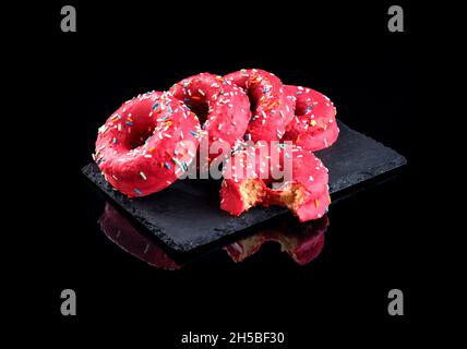 Stack of pink donuts decorated with colorful sprinkles on a black stone plate Stock Photo