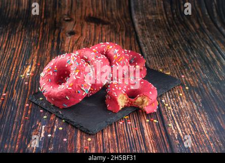 Stack of pink donuts decorated with colorful sprinkles on a black stone-plate Stock Photo