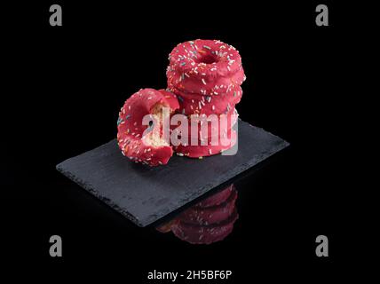 Bunch of pink donuts decorated with colored sprinkles on a black stone plate with a black background Stock Photo