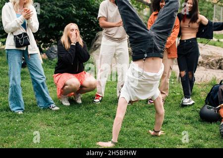 Male teenager doing handstand by friends in park Stock Photo