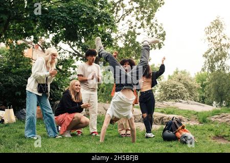 Multiracial friends cheering teenage boy doing handstand at park Stock Photo