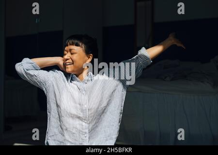 Smiling woman stretching in bedroom at home Stock Photo