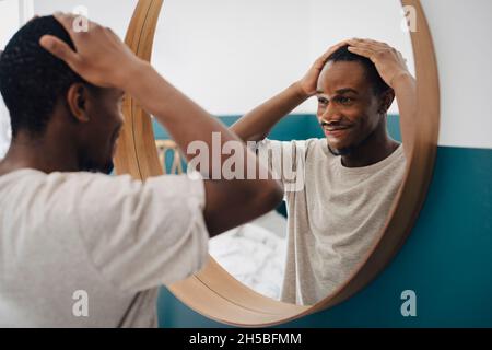 Smiling man with hand in hair looking in mirror at home Stock Photo
