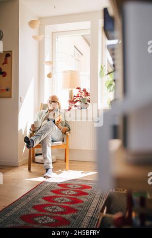 Senior man reading book while having coffee by window at home Stock Photo