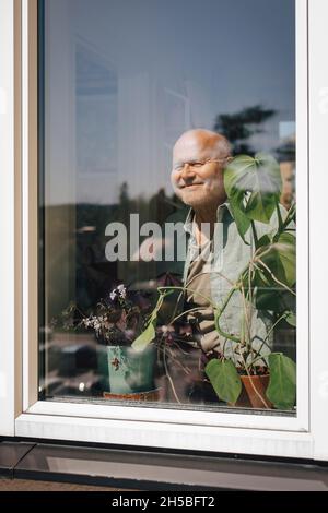 Smiling senior man looking through window on sunny day Stock Photo