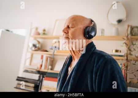 Senior man listening music with eyes closed through headphones at home Stock Photo