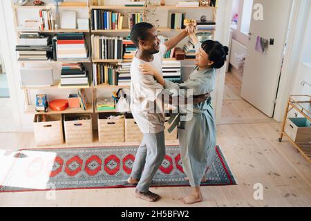 Smiling multiracial couple dancing together in living room at home Stock Photo