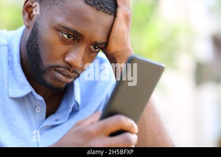 Worried man with black skin checking smart phone content in the street Stock Photo
