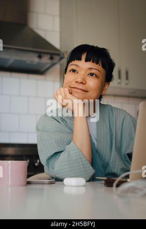 Young woman day dreaming with hand on chin in domestic kitchen Stock Photo
