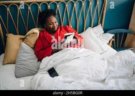 Smiling woman reading book on bed at home Stock Photo