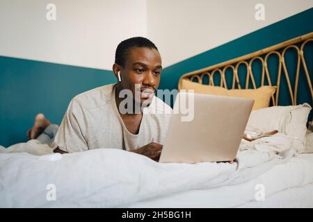 Mid adult man using laptop over bed in bedroom Stock Photo