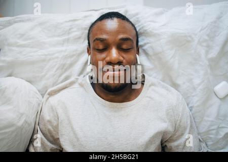 Smiling man wearing wireless in-ear headphones while relaxing with eyes closed Stock Photo
