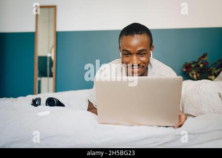 Smiling mid adult man using laptop while lying on bed at home Stock Photo