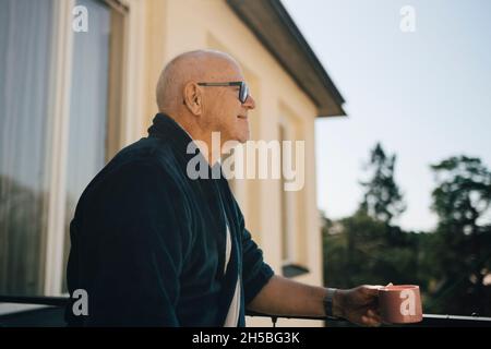 Smiling senior man looking away while holding coffee cup in balcony Stock Photo