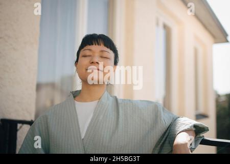 Young woman standing with eyes closed in balcony Stock Photo