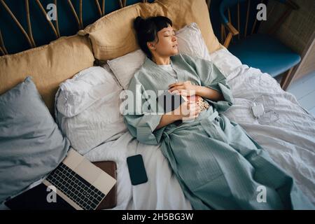 Directly above view of young woman sleeping with book on bed Stock Photo