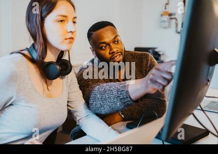 Male hacker discussing with female colleague over computer in startup company Stock Photo