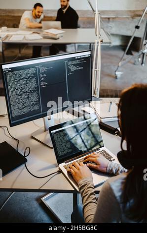 Female programmer coding on laptop at table in creative office Stock Photo