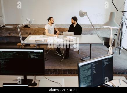 Smiling male colleagues talking while sitting at table in office Stock Photo