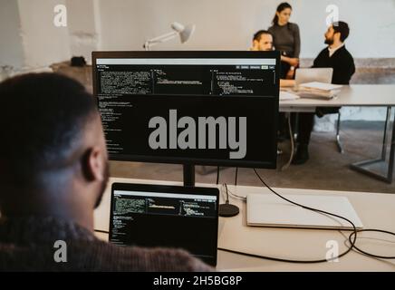 Male programmer coding on computer and laptop in startup company Stock Photo