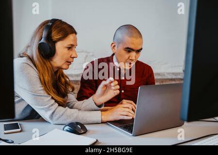 Mature female hacker discussing with male colleague over laptop at creative office Stock Photo