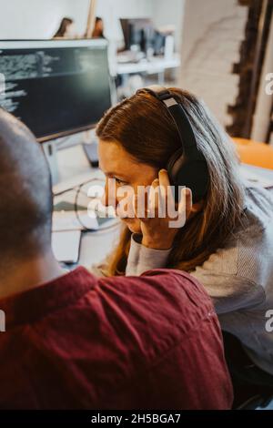 Female programmer listening through headphone while doing coding at startup company Stock Photo