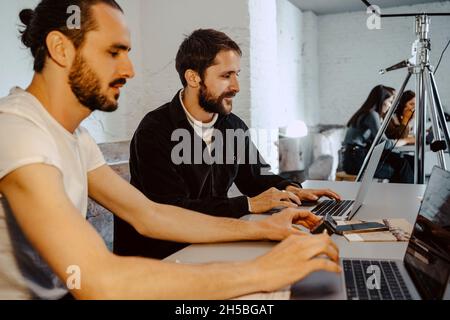 Male hackers working on laptops at desk in creative office Stock Photo