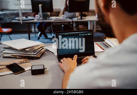Male programmer coding on laptop at desk in startup company Stock Photo