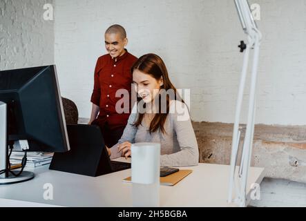 Smiling female hacker using laptop while working with colleagues at startup company Stock Photo