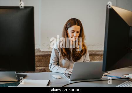 Mature female programmer working on laptop in office Stock Photo