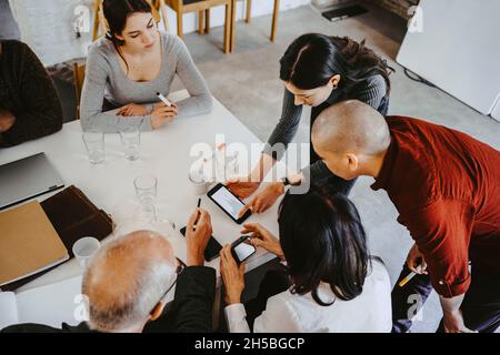 High angle view of female hacker discussing over smart phone with advisors at office Stock Photo