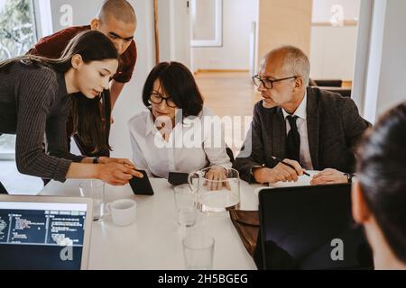 Male and female programmers discussing over smart phone with board of directors at office Stock Photo