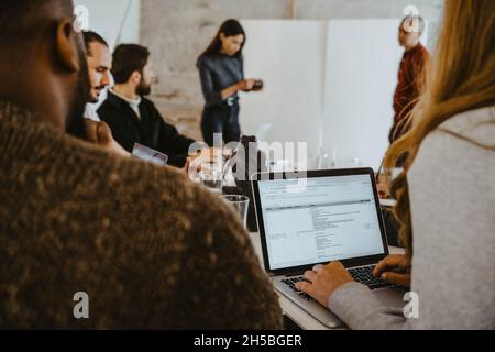 Female programmer using laptop during meeting with colleagues in office Stock Photo