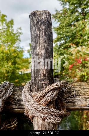 Dirty gray and black wooden beams connected with rough rope made of hemp, concept with blurred bokeh background Stock Photo