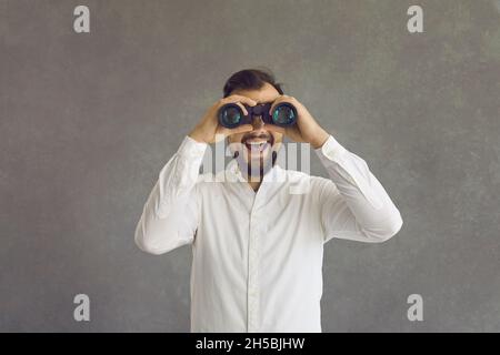 Young man looking through binoculars over grey studio background with happy face Stock Photo