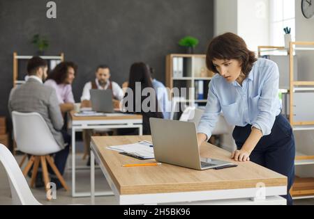 Young caucasian woman secretary using laptop while team having briefing Stock Photo