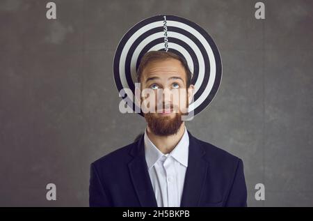 Pensive businessman stands on the background of a game of darts hanging on the wall. Stock Photo