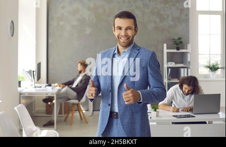 Happy employee or business leader standing in office, smiling and giving thumbs up Stock Photo