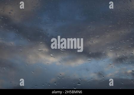 Raindrops on a window with white and gray clouds and some blue sky in the background. Landscape orientation. Stock Photo