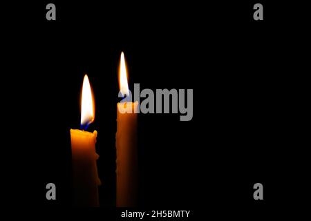Two burning candles in the darkness. Burning yellow candles on black background with copy space. Stock Photo