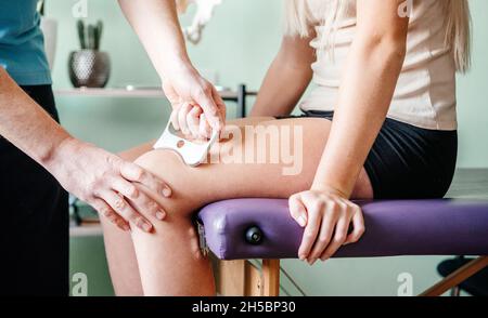 Therapist using IASTM instrument treatment, girl receiving soft tissue treatment on her leg with guasha stainless steel tool Stock Photo