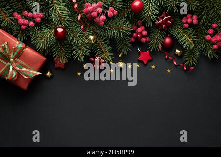 Black Christmas background with Christmas tree branches and red berries, winter festive composition with copy space. Top view. Stock Photo