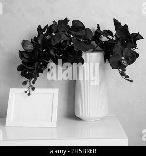 Orchid flowers in vase and photoframe on cabinet by wall Stock Photo