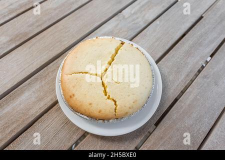 Whole plain cheese cake cheesecake on plate at home wooden table background with cracked cracks cooking fail due to temperature Stock Photo