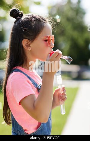 child girl blowing soap bubbles in park. Stock Photo