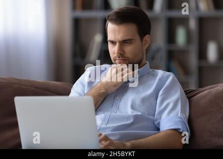 Thoughtful young man looking at laptop screen. Stock Photo