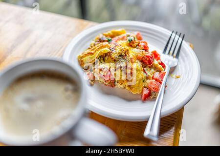 Homemade plate with cooked omelette amde with tomatoes, cilantro and red peppers vegetables on wooden kitchen table with fork, cup of coffee drink in Stock Photo