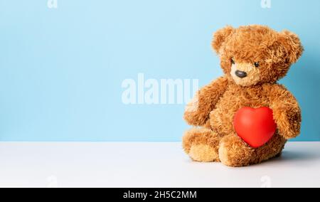 Teddy bear holding a heart on a background. Valentine's Day. Stock Photo
