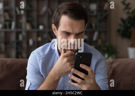 Thoughtful young man looking at cellphone screen. Stock Photo